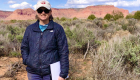 Photo of woman standing in field of desert vegetation with flat-topped mesas in the background.