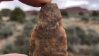 Photo showing a worked stone artifact held between thumb and forefinger with landscape in the background.