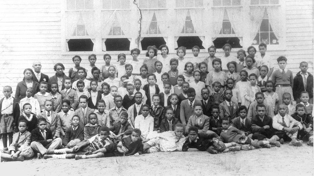 Black and white photo of African American students outside the windows of a building.