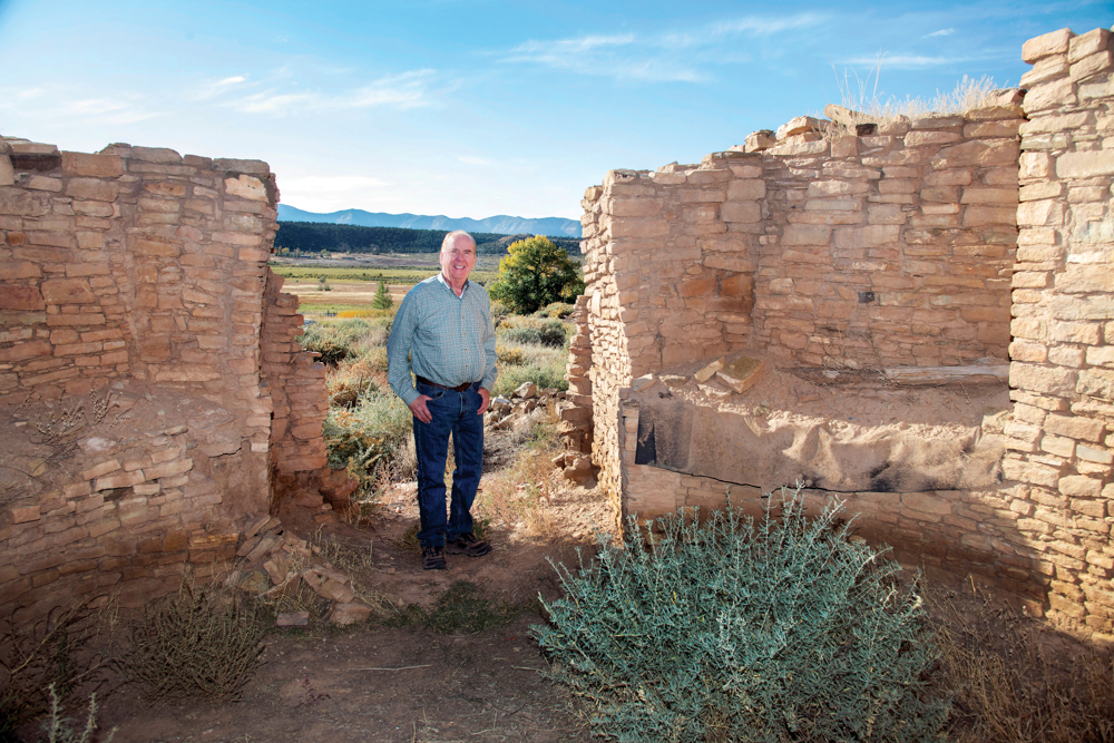 A man stands in an opening between two sections of stacked stone walls.