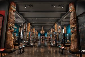 Photo of dimly lit exhibit hall lined with carved totem poles.