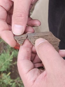 Closeup view of a person's hands holding two sherds of pottery that appear like they may have belonged to the same vessel.